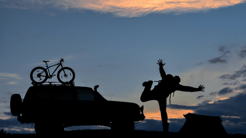 silhouette of a person kicking with their car and camping tent in the background