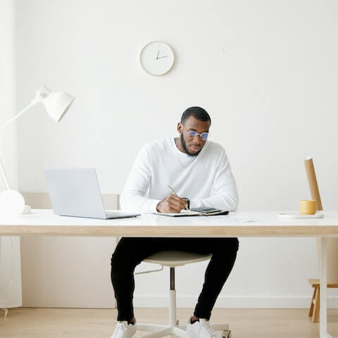 Creative entrepreneur sat at his desk writing in his planner