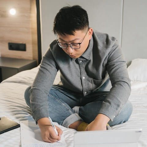 Entrepreneur journalling in a planner whilst sat on his bed