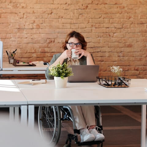 Lady in wheelchair working at her desk drinking a cup of coffee