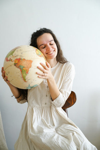 woman in white dress holding globe, smiling