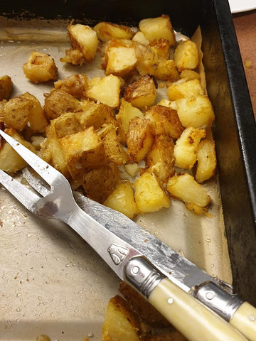Oven dish with roasted potatoes and a carving knife and fork resting on it