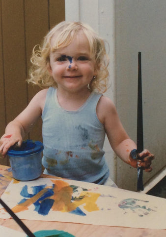 3 year old girl holding a paintbrush with an artwork and covered in paint 1990s
