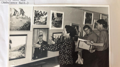 black and white photo of a woman hanging a painting in an art exhibition for Cambridge Art Society - Mary MacBeath