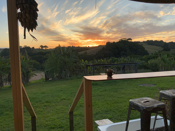 The sun setting over farmland from the view of a deck with a cup of tea and a bunch of bananas hanging in the twilight.