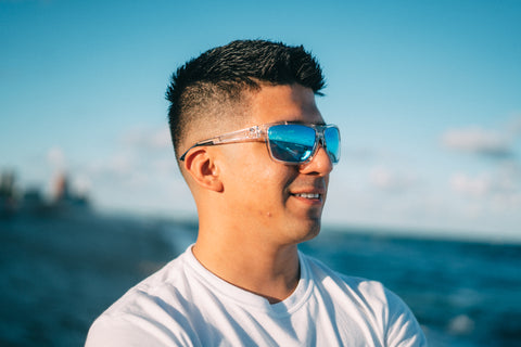 a man wearing Torege polarized sunglasses standing by the beach smiling