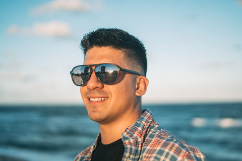 a man standing by the beachside smiling wearing Torege retro-inspired sunglasses