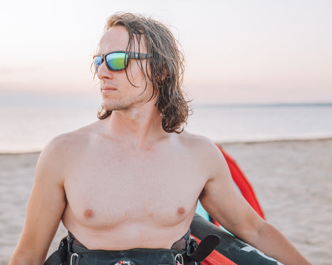 a man holding a surf kite on the beach wearing Torege water sports sunglasses