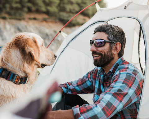 a man sitting beside of a camp enjoying time with his dog wearing Torege polarized sunglasses