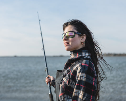 a woman angler holding a fishing rod standing by the sea wearing Torege polarized fishing sunglasses