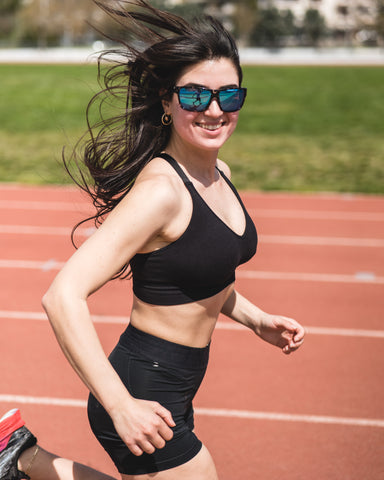 a woman running on the track smiling wearing Torege running sunglasses