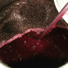 image shows red wine undergoing a punch down maceration technique in a steel vat