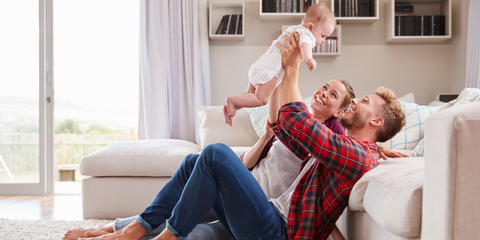 Parent lifting baby in air joyfully in living room with door open