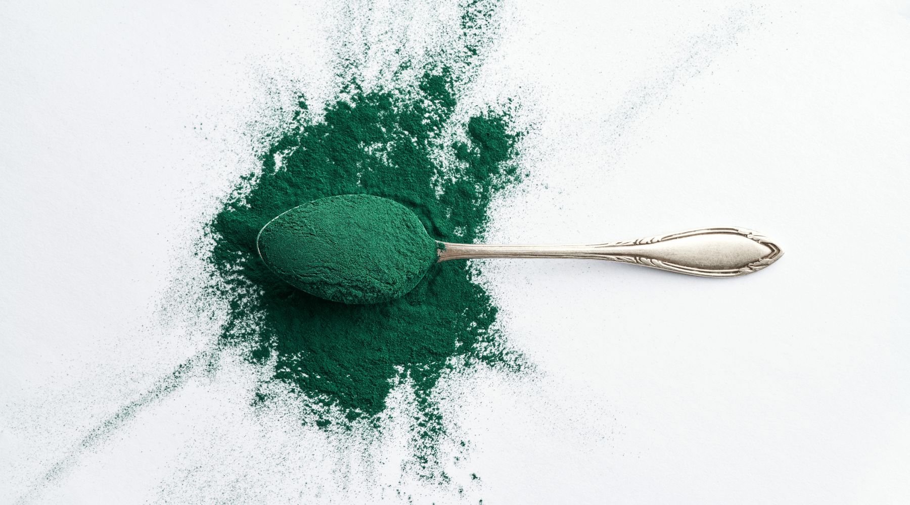 Grünes Spirulina-Pulver mit einem Vintage-Löffel auf weißem Hintergrund