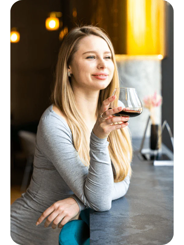 Donna bionda che beve vino da un bicchiere Aequilibrium di Audacem, evidenziandone il design elegante