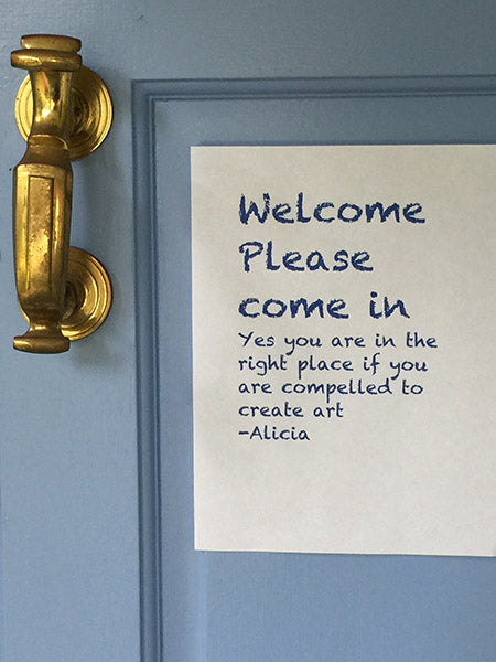 Paper sign on door with text that reads, "Welcome. Please come in. Yes, you are in the right place if you are compelled to make art."