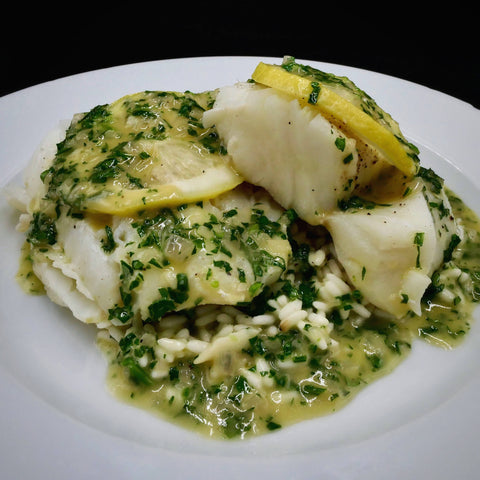 poached fresh cod topped with lemon herb butter sauce on a white plate