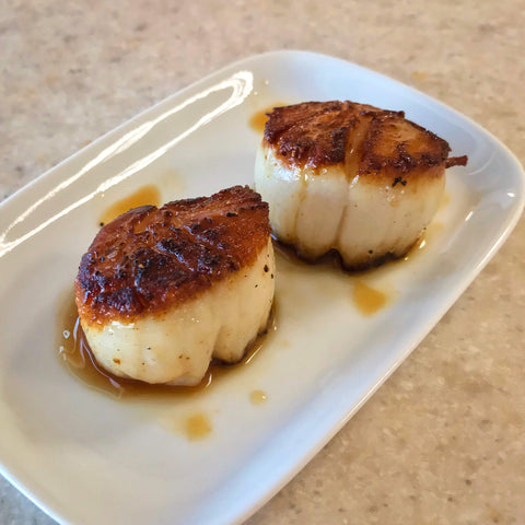 two caramelized seared scallops on a small rectangular plate