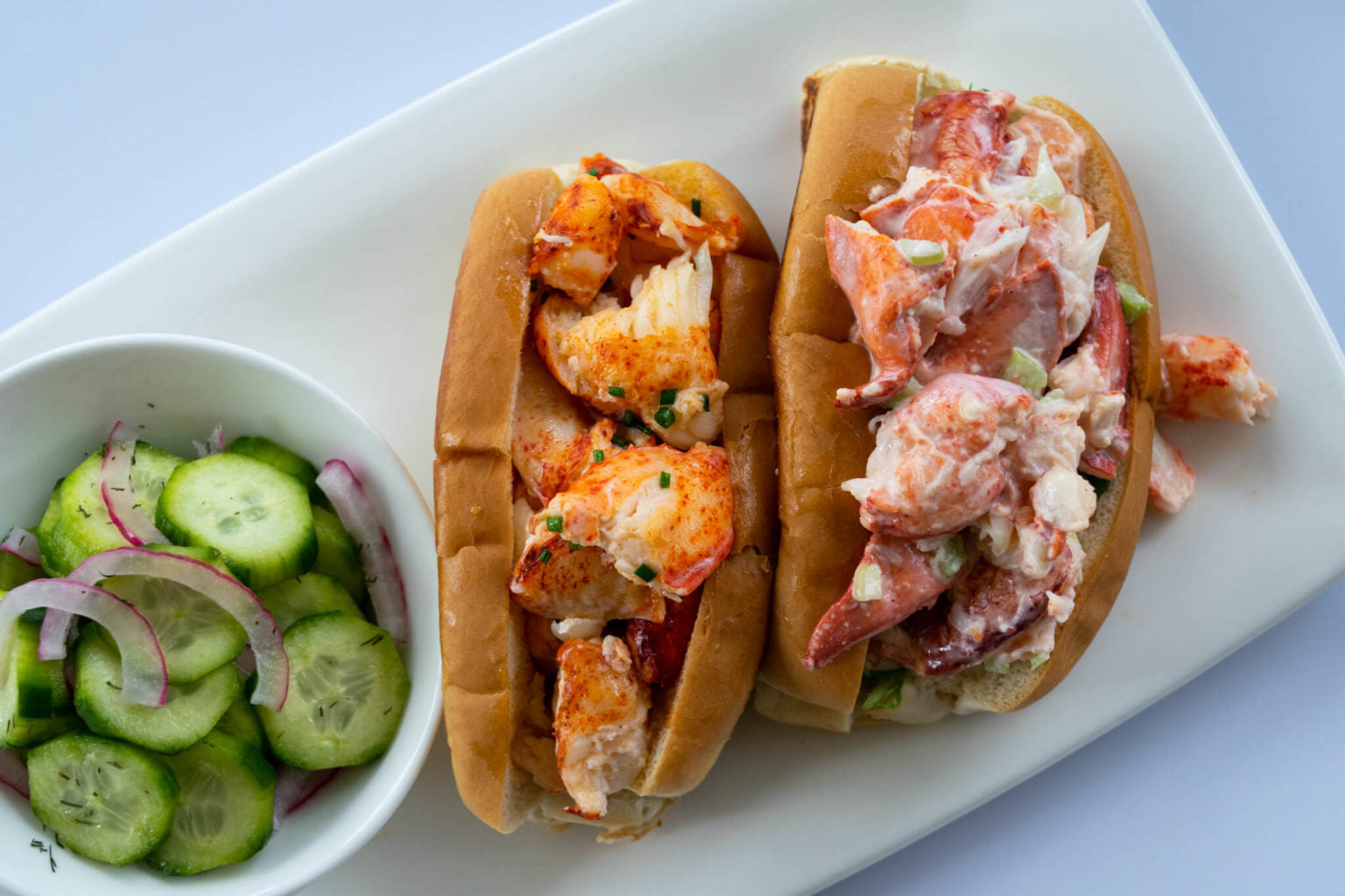 warm lobster roll with butter next to a cold lobster roll with mayonnaise on a white plate