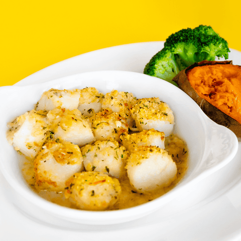 baked scallop casserole in a white dish with broccoli and sweet potato on the side