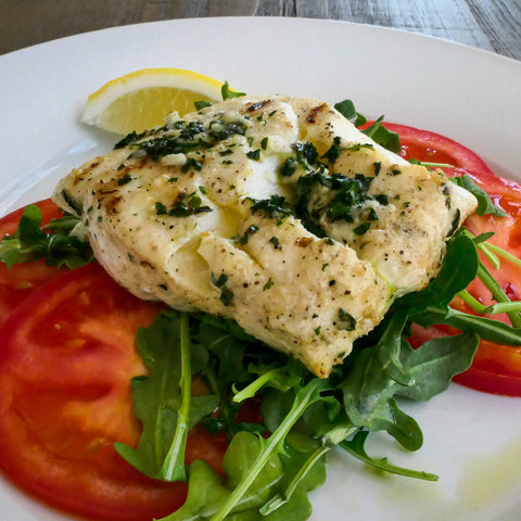 6 ounce portion of baked cod on a bed of arugula and tomatoes on a white plate