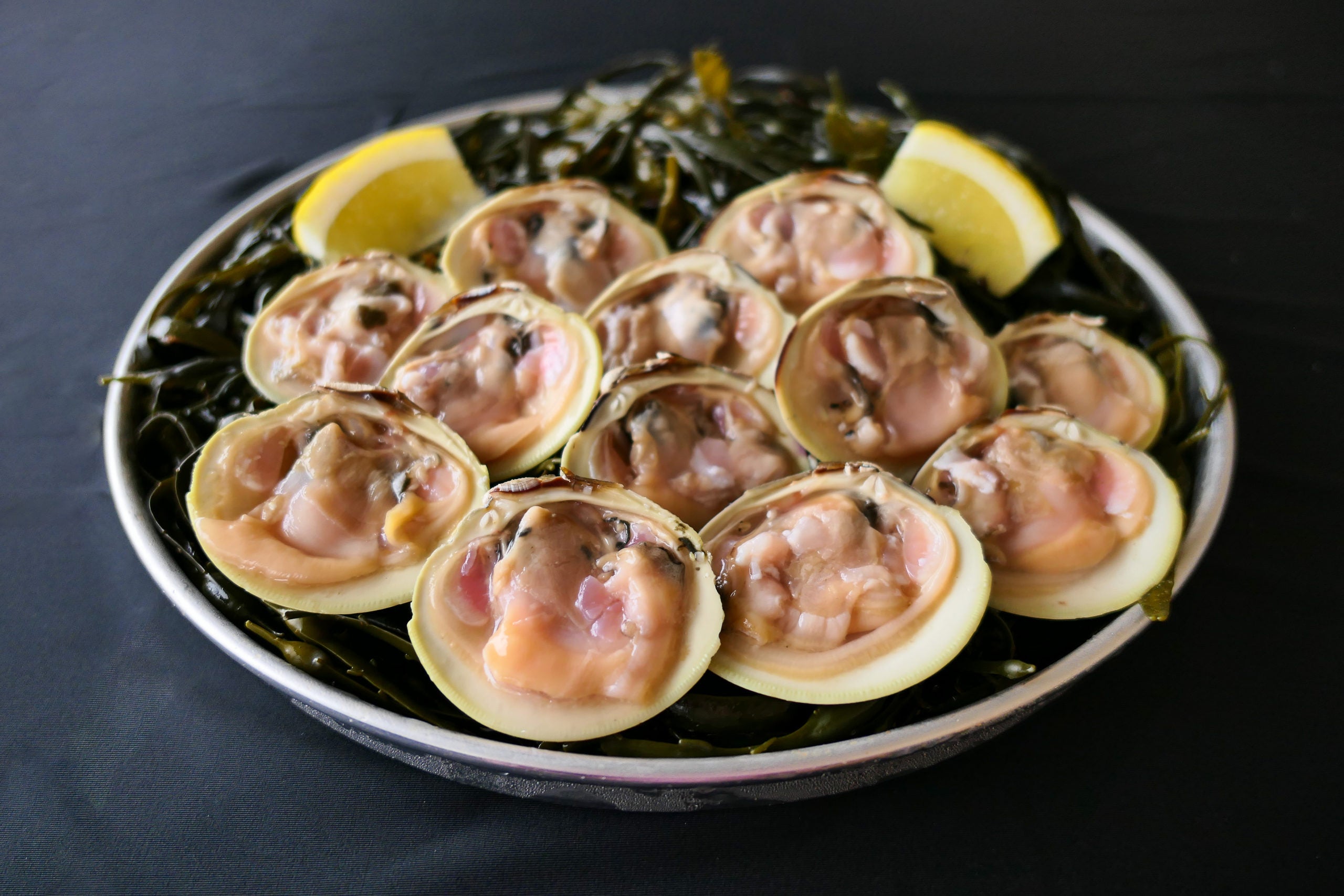 shucked littleneck clams on the half shell with lemon on a bed of seaweed