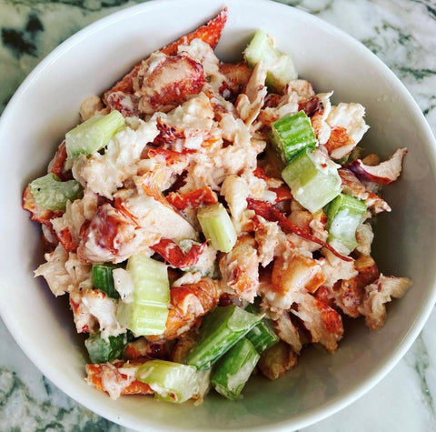 lobster salad with lettuce, celery, and avocado in a white bowl on a granite countertop