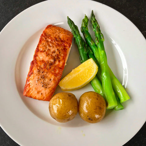 pan seared salmon with asparagus, roasted potatoes, and a lemon wedge on a white plate