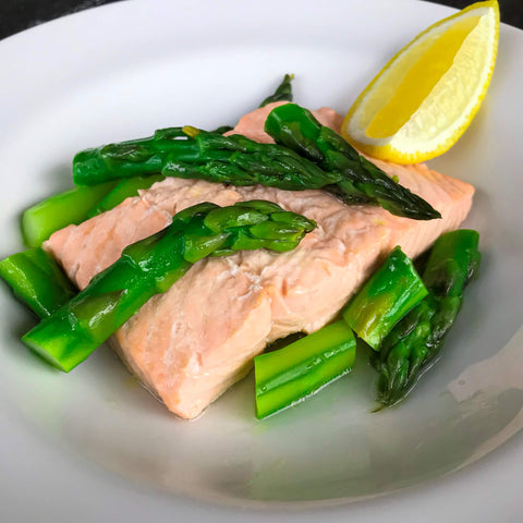 poached salmon with asparagus and a lemon wedge in a white bowl