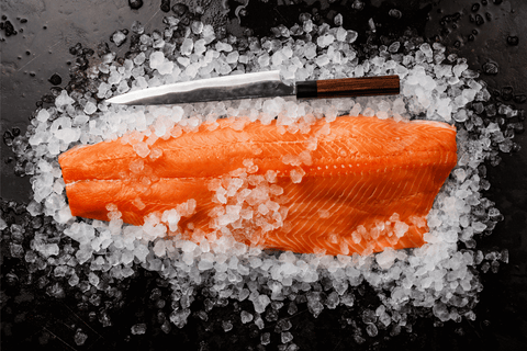 fresh salmon fillet on a bed of ice with a fish cutting knife above it