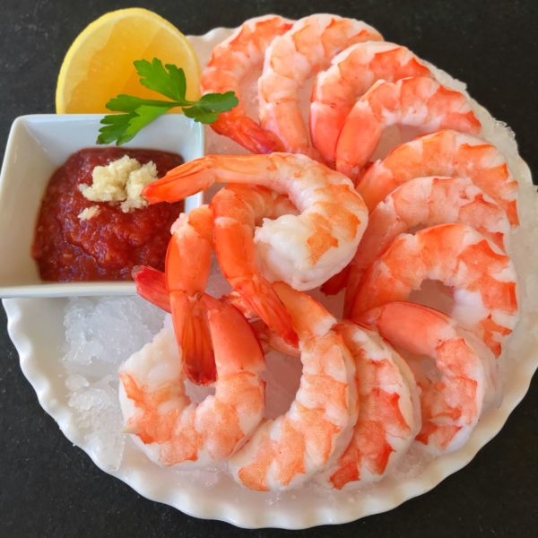 12 pieces of cooked shrimp on an ice covered plate with lemon and cocktail sauce on the side