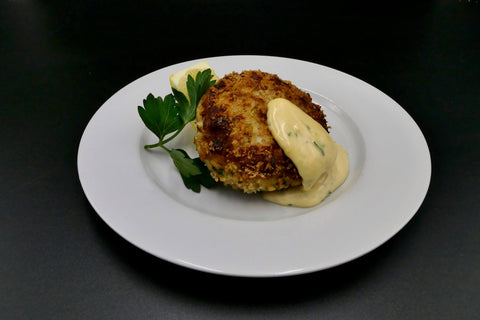 large Maryland style crab cake on a white plate topped with a dollop of siracha aioli 