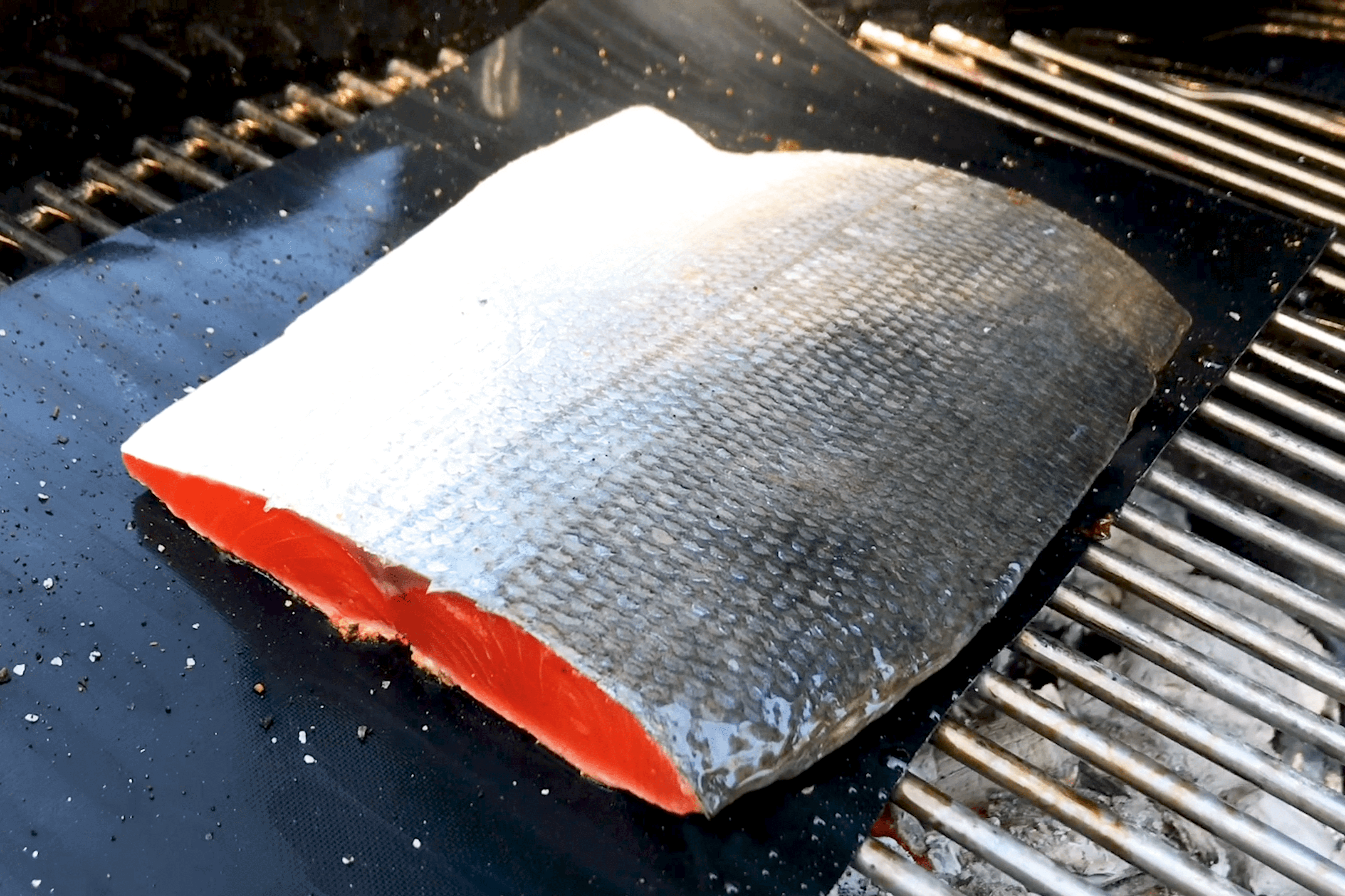 a one pound wild salmon portion skin side up on a grill mat on a charcoal grill