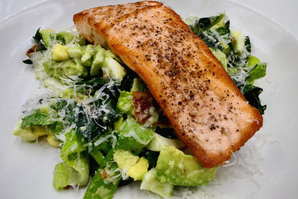 Crispy Pan Seared Salmon on top of a fresh Caesar salad in a bowl