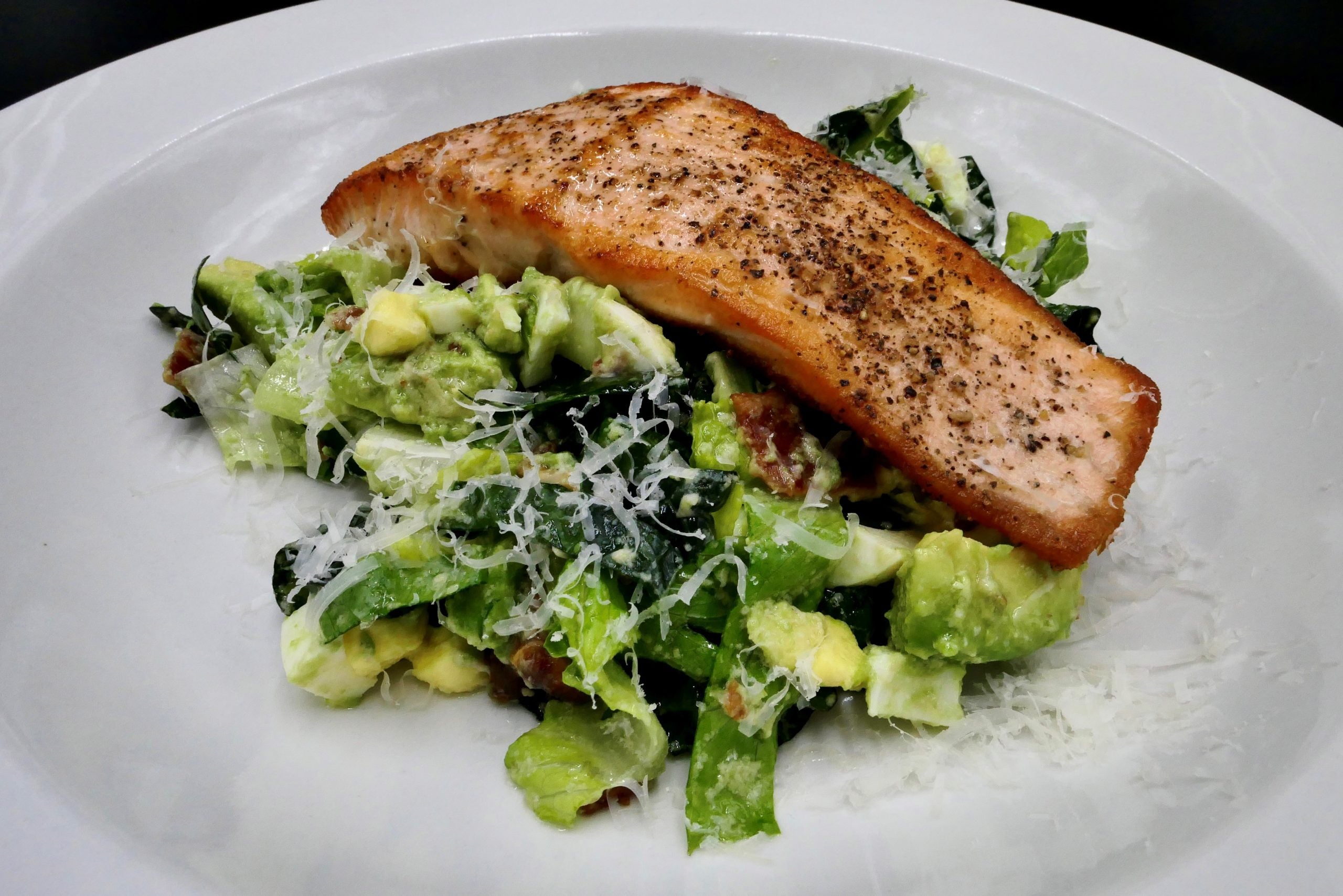 Caesar Salad topped with crispy salmon fillet in a white bowl