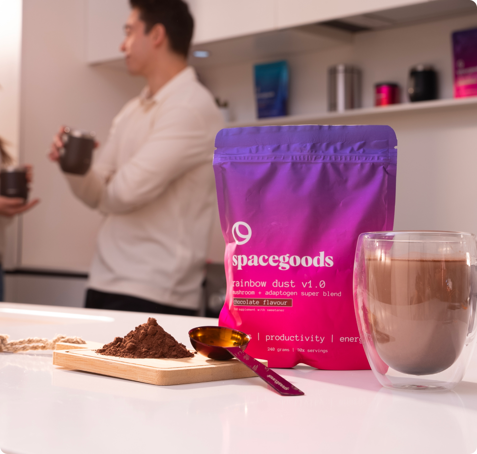 Packaged superfood powder on table with cup and man in background.