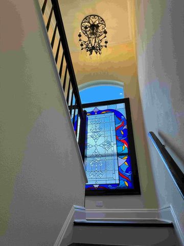 An image looking up a stairwell which features a stained glass window and a chandelier