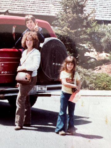 Young Elli Milan standing with her mom and brother next to a red Ford Bronco