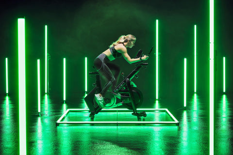 Girl in grey gym wear cycling on a green-lit RE:GEN