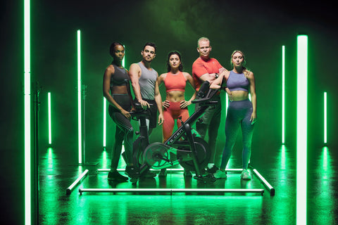 Group in gym wear standing next to the RE:GEN bike on a green lit platform