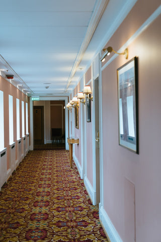 Carpeted hotel corridor with windows on the left hand side and bedroom doors on the right