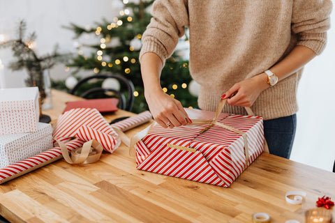 Female in camel colour sweater wrapping a box in red and white striped paper