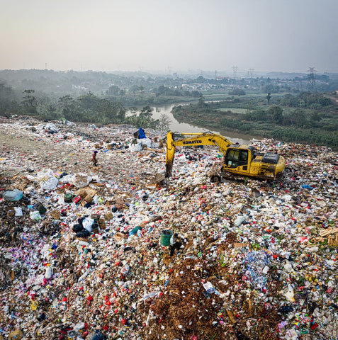 Landfill with yellow digger and city in the background