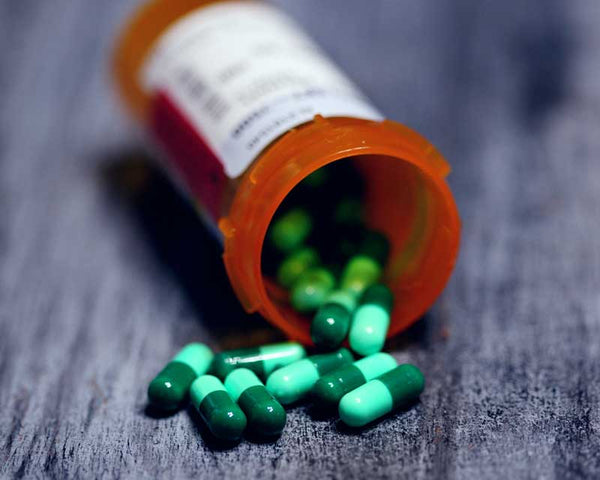 Overturned prescription bottle of green capsules on grey floor
