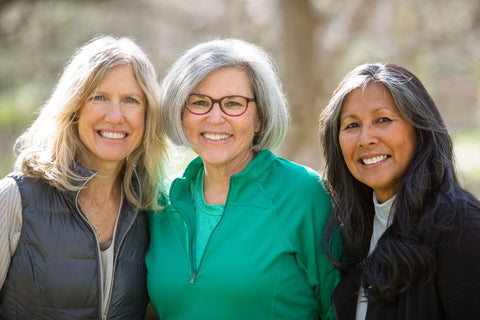 Three older women outside with arms wrapped around each other and smiling