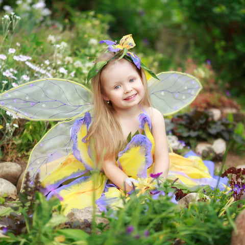 Little girl smiling dressed as a fairy sitting in garden