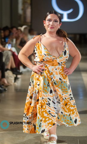A petite brunette woman, standing at under 4ft 11, is dressed in an A-line patterned dress featuring a combination of white, black, sage, and orange hues.