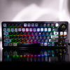 The keycaps on the Gamakay LK75 keyboard are showcased with a full spectrum of backlighting. The keycaps themselves have a diverse color palette, with each row or cluster of keys featuring a different hue, such as teal, purple, or yellow. The icons and sy