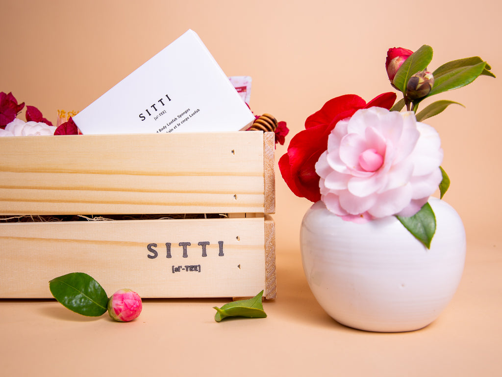wooden Beaux Box with the "SITTI" logo in black in the bottom right-hand corner; a short white ceramic vase of flowers sits to the right with pink and red camelias inside.