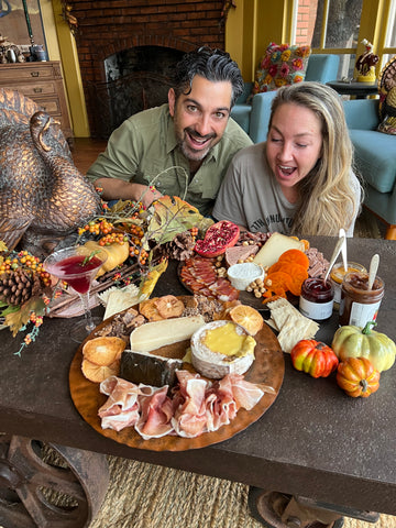 Two adults behind three cheese trays decorated for the thanksgiving holiday